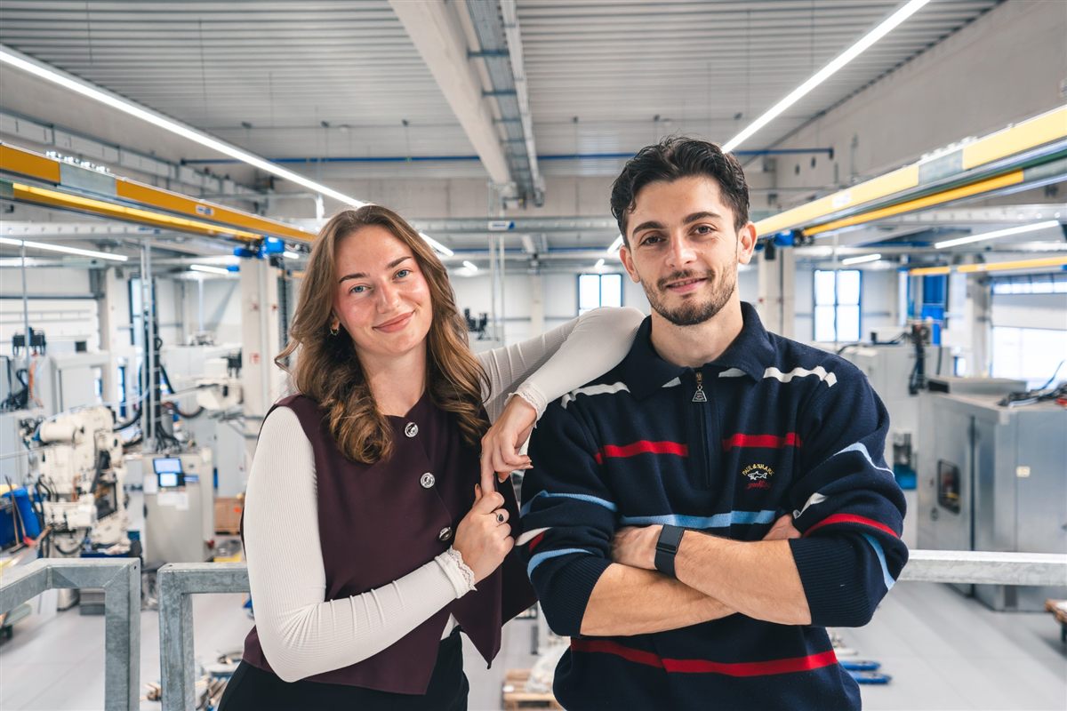 Michelle und Adrian in einer großen Produktionshalle mit Maschinen im Hintergrund